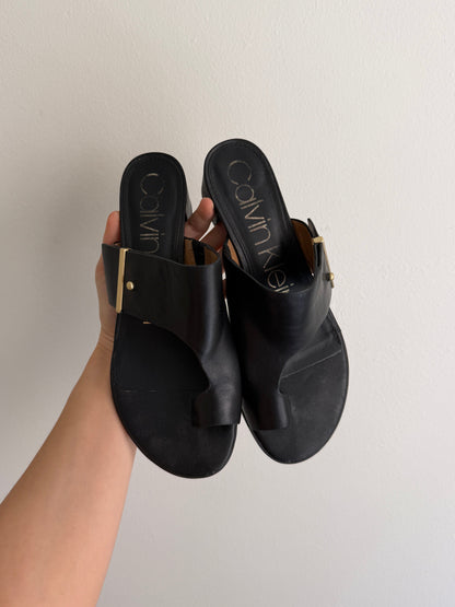 Black sandals held by a hand against a plain background