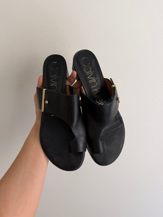 Black sandals held by a hand against a plain background