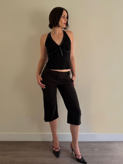 Woman wearing a black halter top and black capri pants against a beige wall.