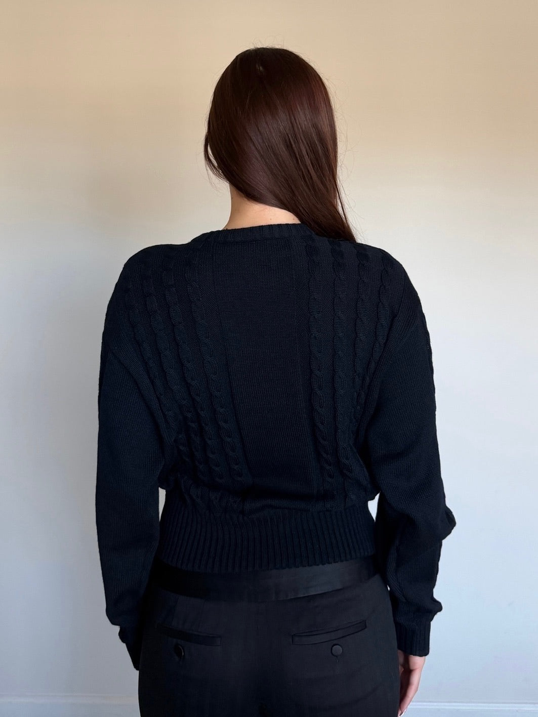 Person wearing a black knit cardigan against a plain background