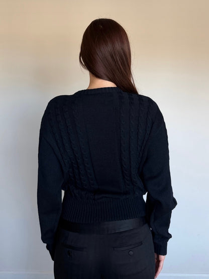 Person wearing a black knit cardigan against a plain background