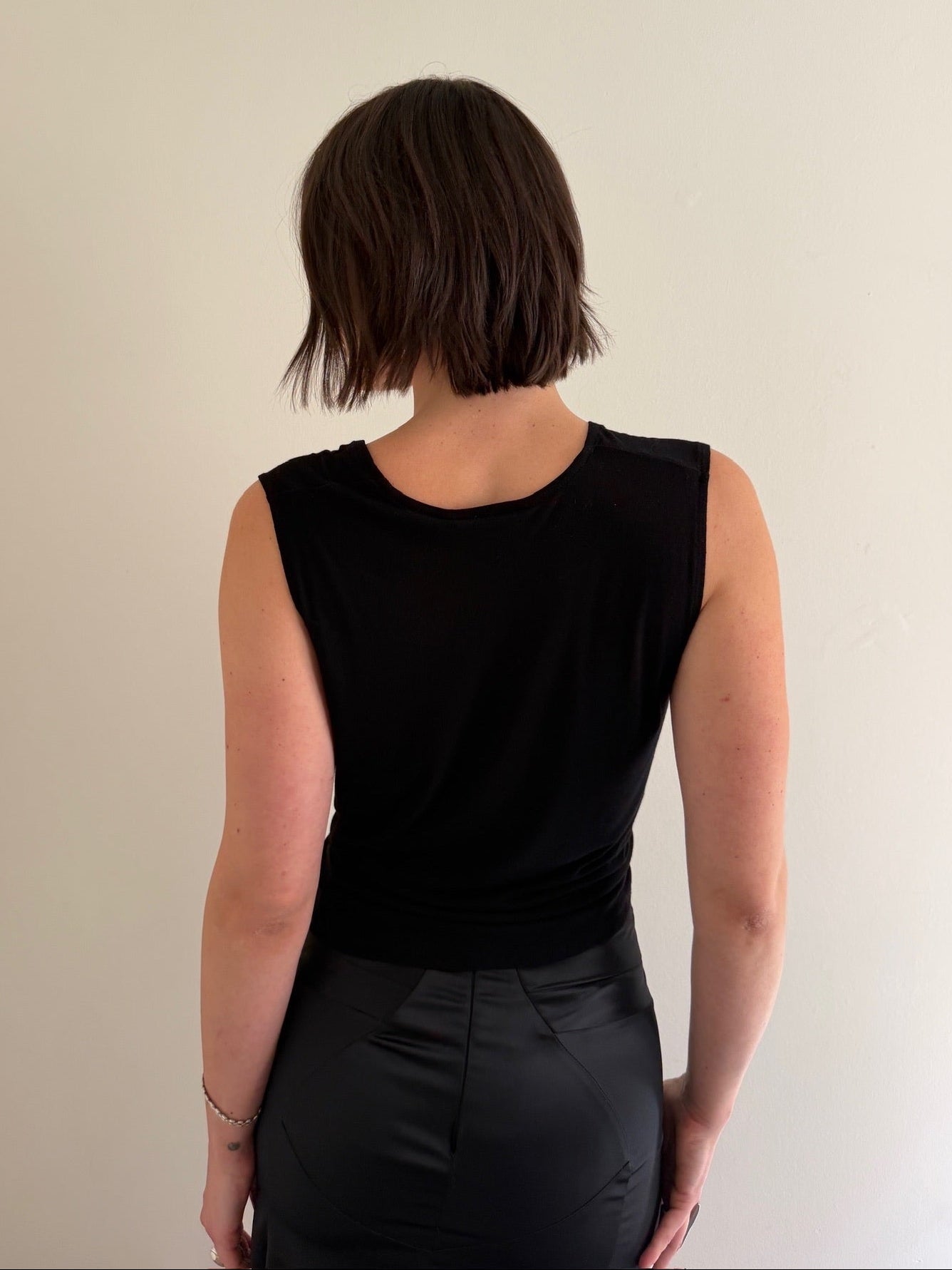 Person wearing a black sleeveless top and black pants against a beige background