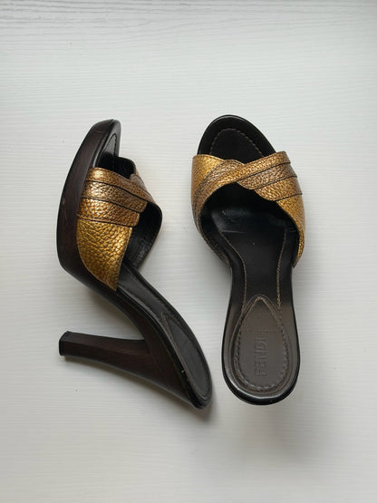 A pair of women's heeled slide sandals with textured gold straps and dark brown soles, displayed on a light gray background.