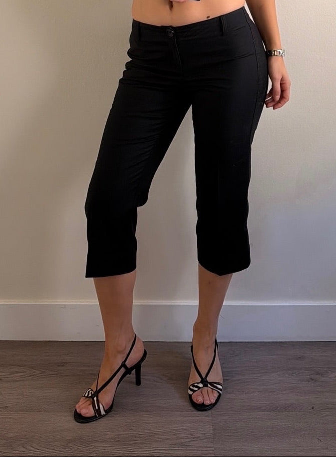 Woman wearing a black outfit standing against a plain wall.