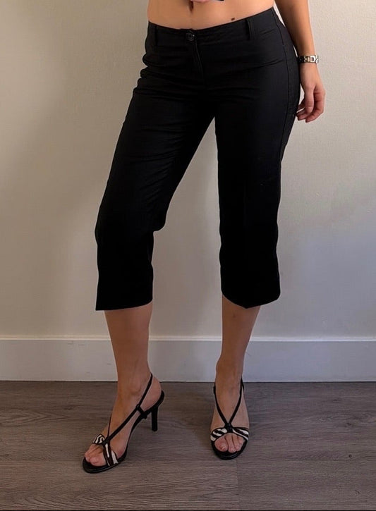 Woman wearing a black outfit standing against a plain wall.
