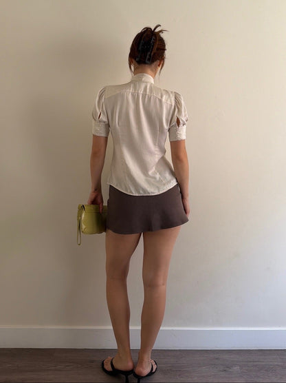 Person wearing a white shirt and brown shorts holding a green bag against a plain wall.
