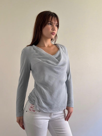 Woman wearing a gray long-sleeve top and white pants against a plain background