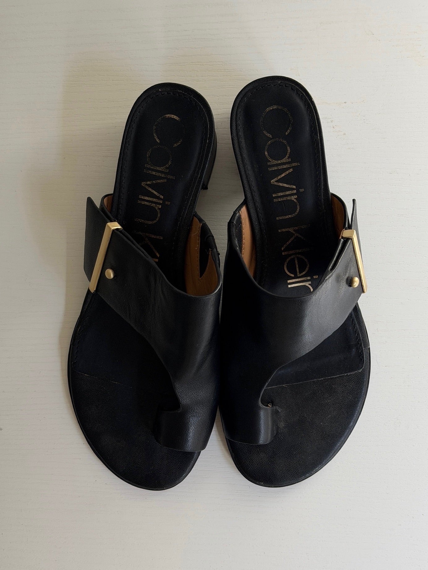 Black sandals with gold accents on a white background