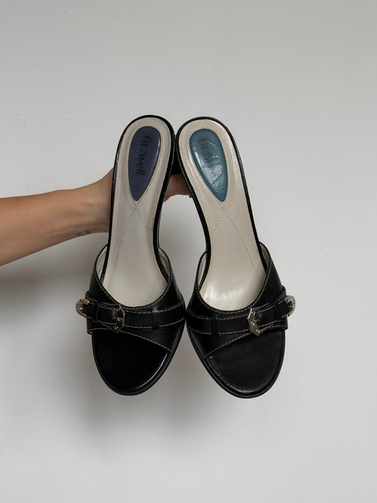 Black high-heeled shoes with a silver buckle on a white background