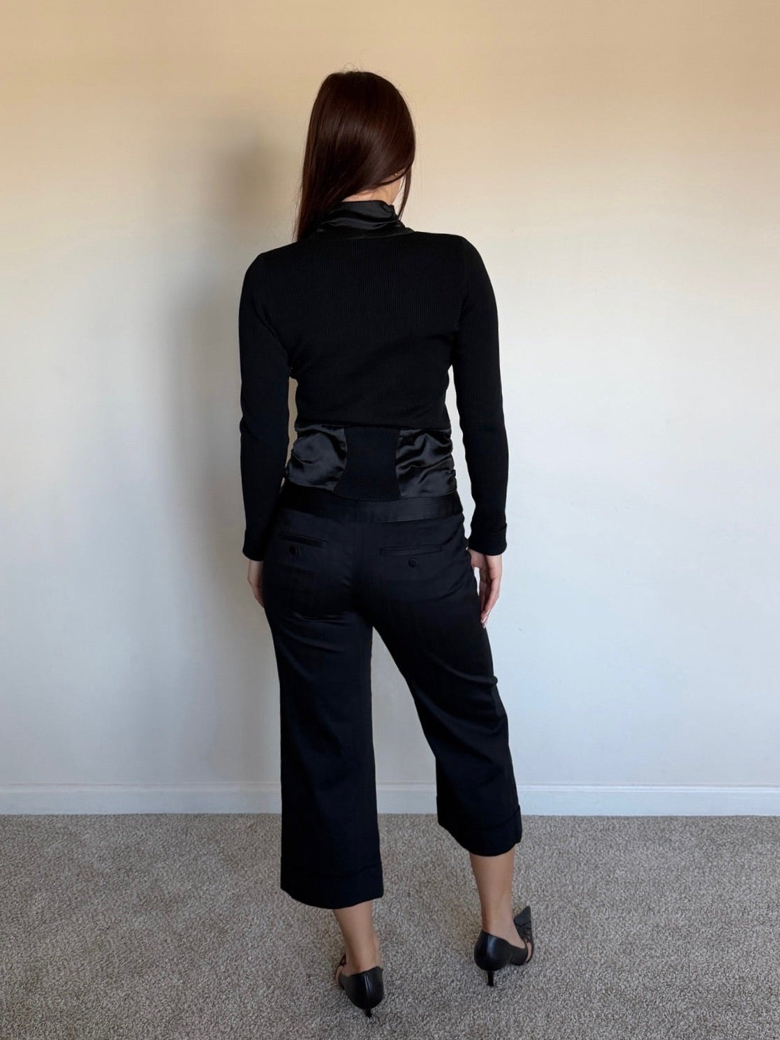 Person wearing a black outfit with a textured pattern against a plain wall.