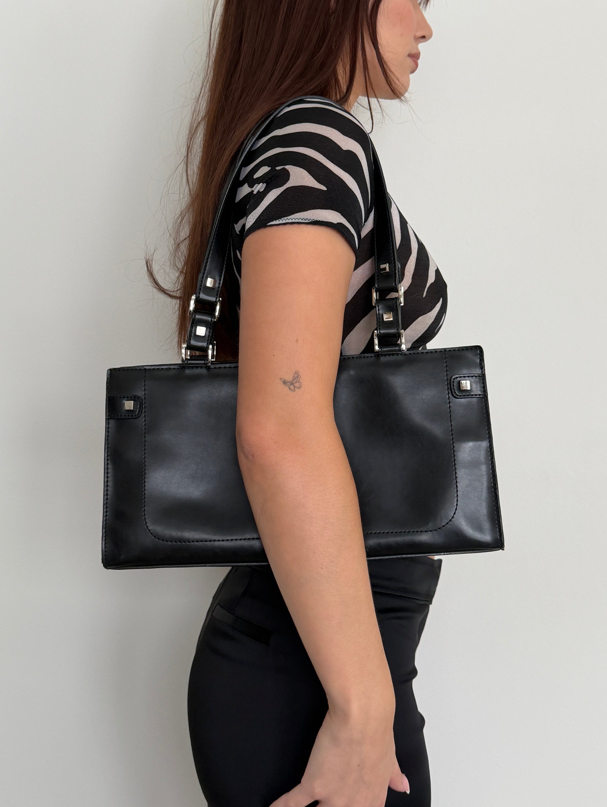 Person holding a black leather clutch bag on a white background