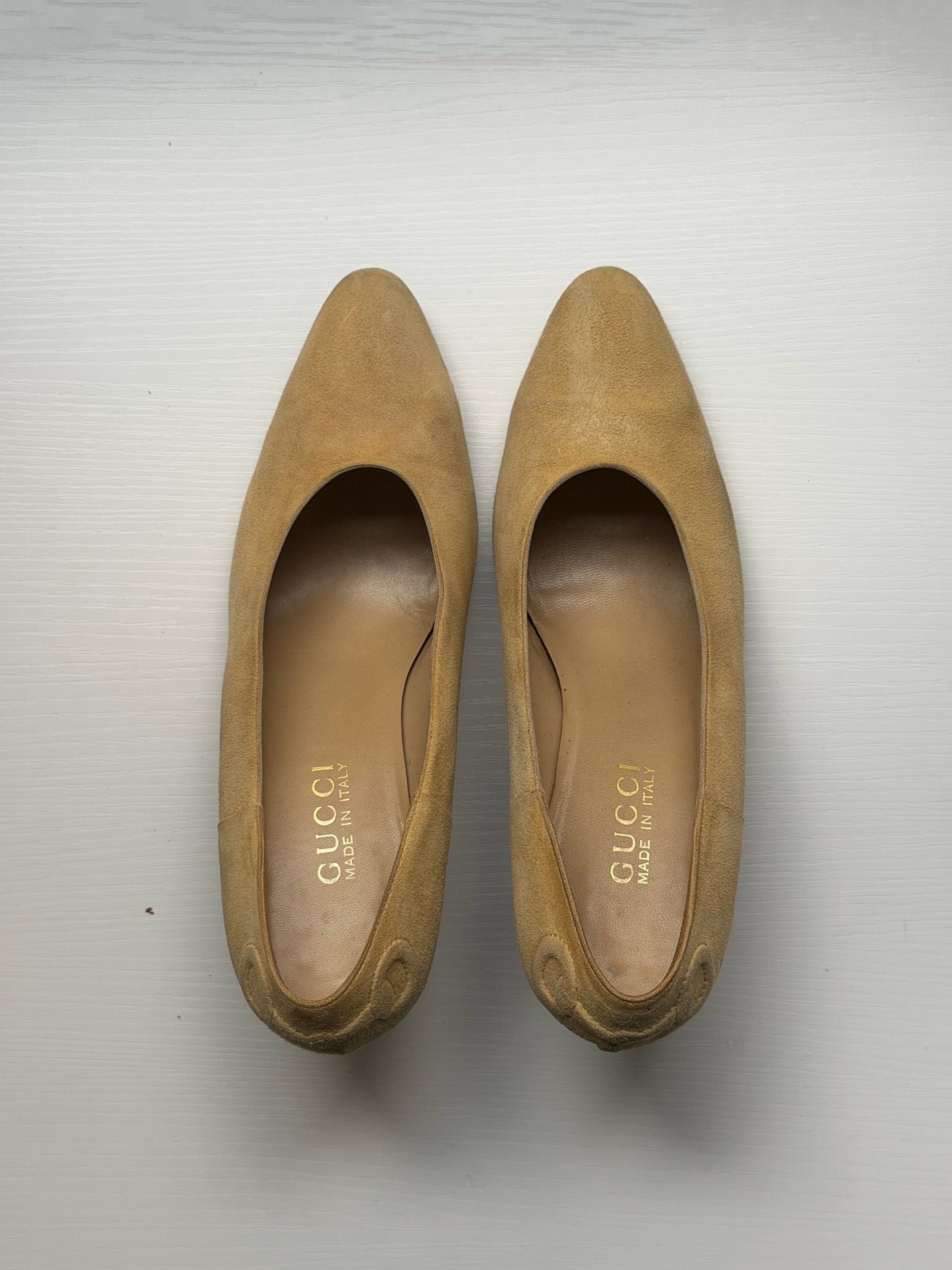 A pair of Gucci suede pointed-toe pumps in a tan color, shown from a top-down view on a light gray background.
