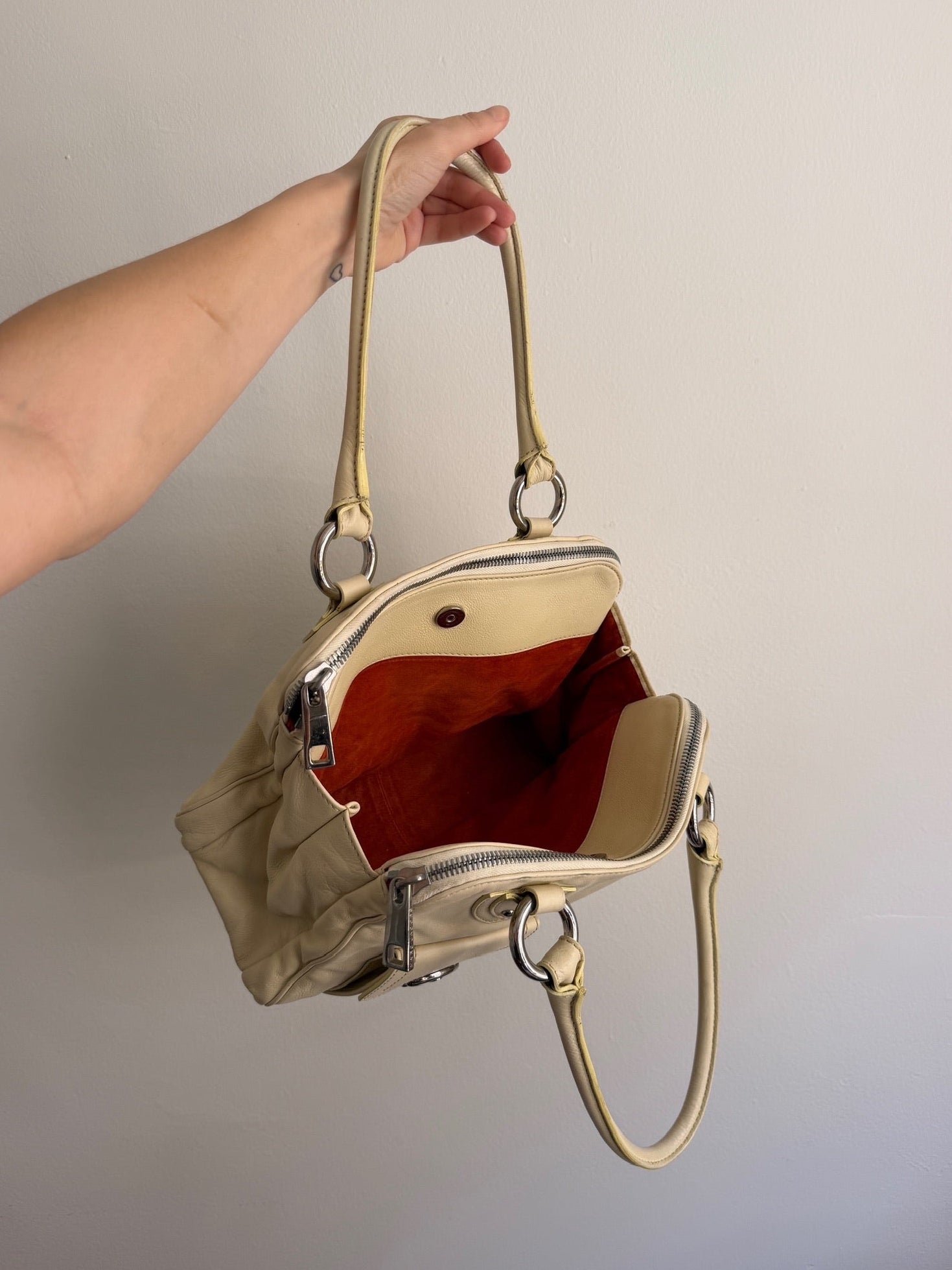 Gold handbag held by a hand against a plain background