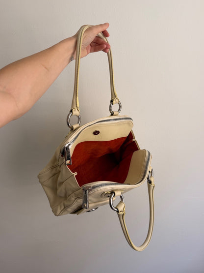 Gold handbag held by a hand against a plain background