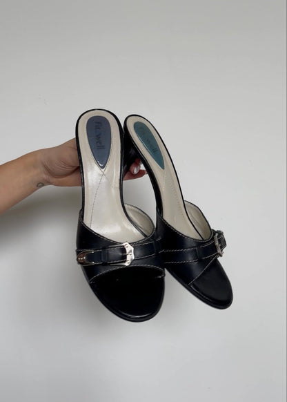 Black high-heeled shoes held by a hand on a light gray background