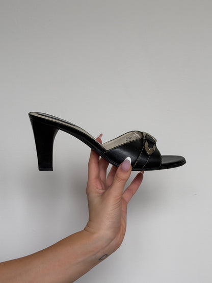 Black sandal held by a hand against a plain background