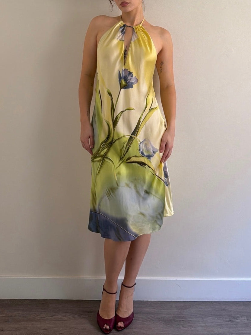 Woman wearing a yellow floral dress against a plain wall.