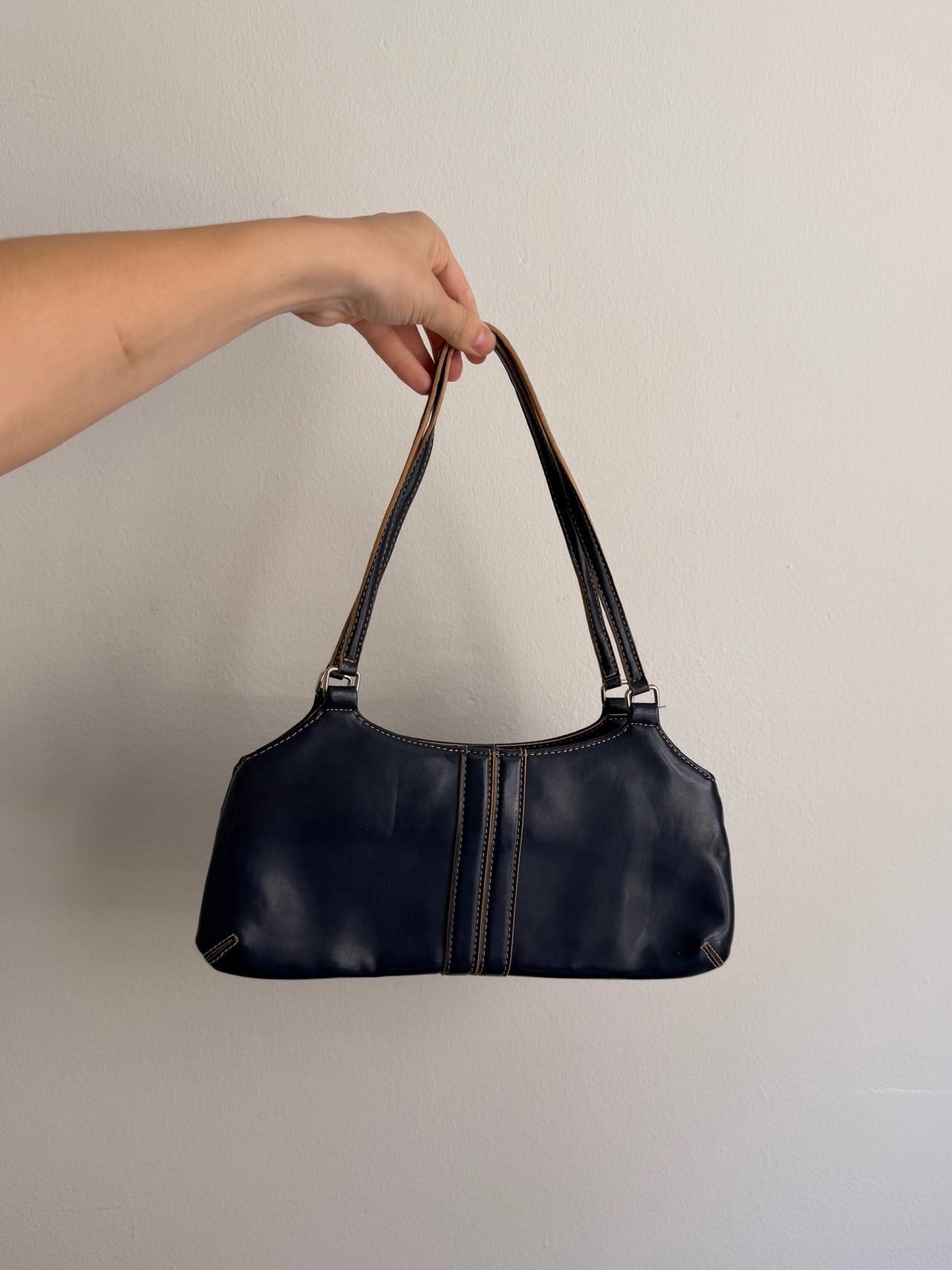 Black handbag held by a hand against a plain background