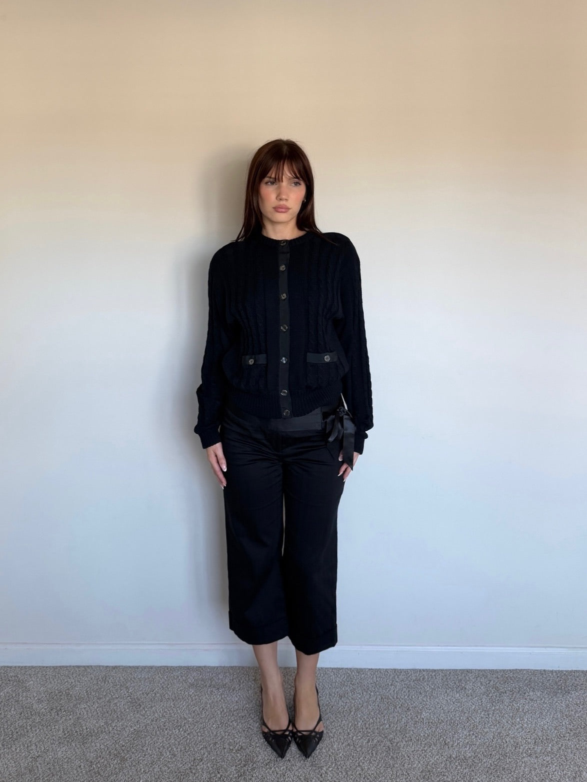 Person wearing a black outfit against a plain wall