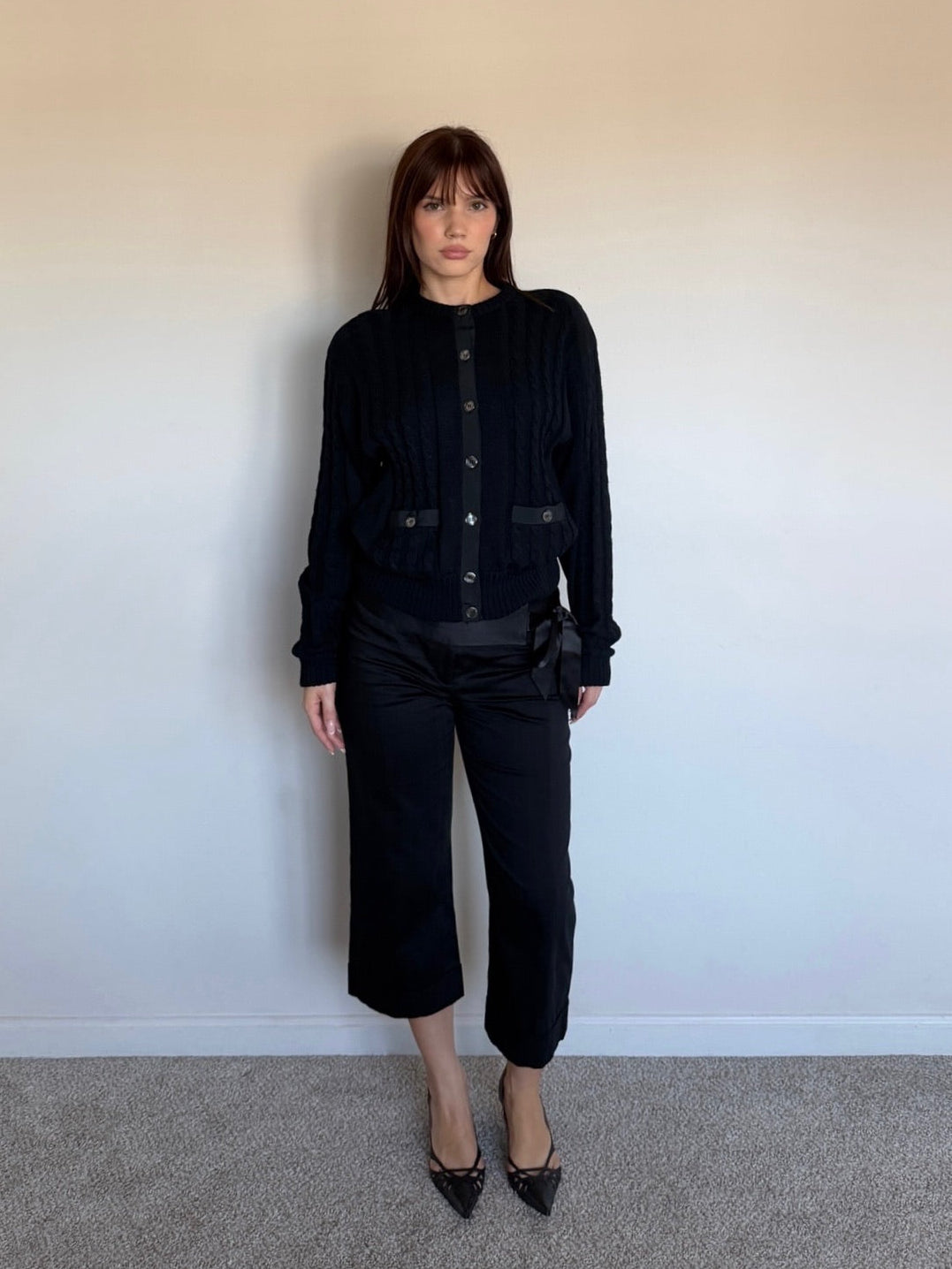 Person wearing a black wool sweater against a plain wall