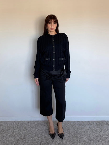 Person wearing a black wool sweater against a plain wall
