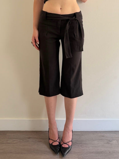 Person wearing black cropped pants with a tie-waist design against a plain wall.