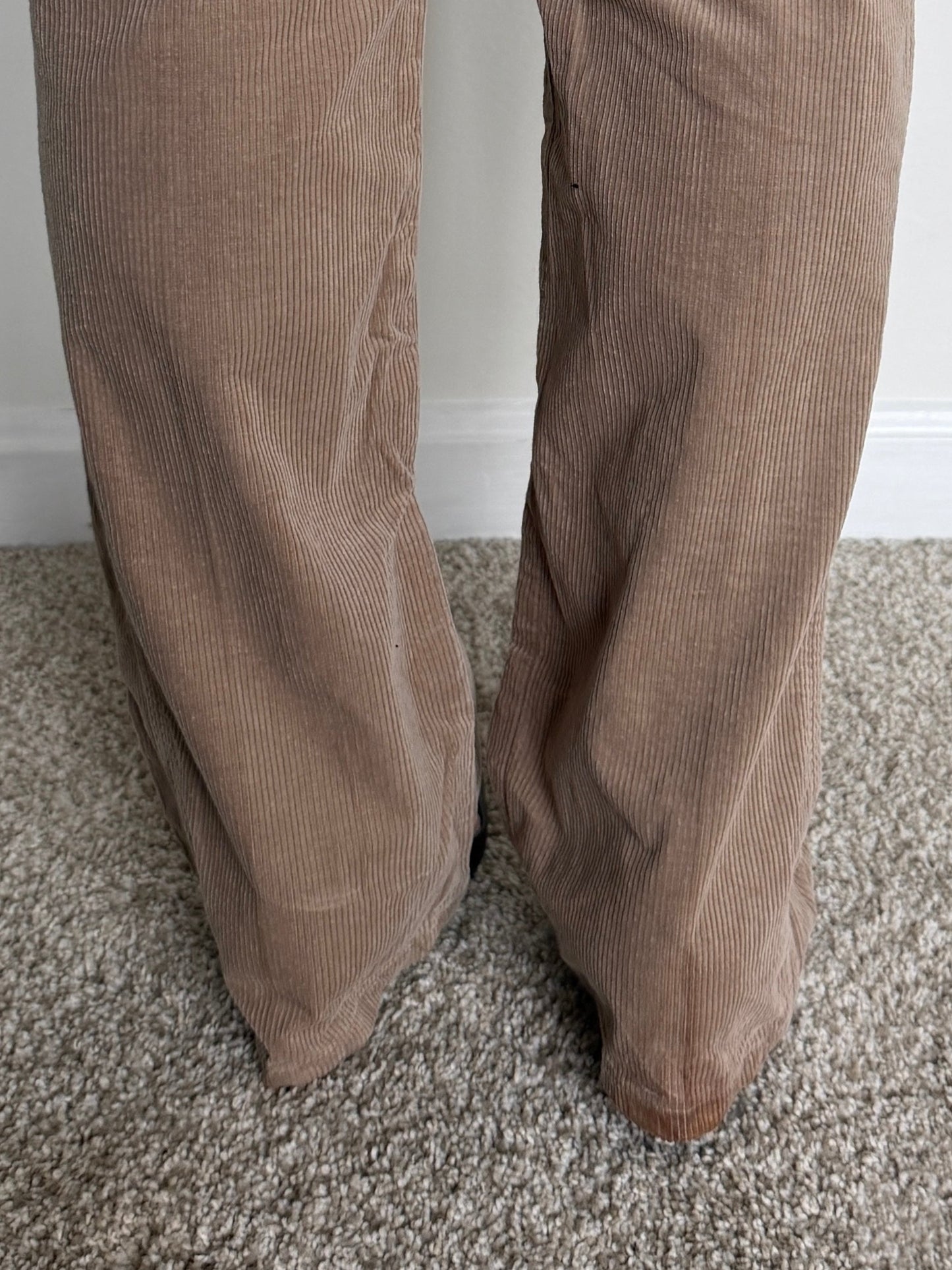 Brown corduroy pants on a carpeted floor with a white wall background