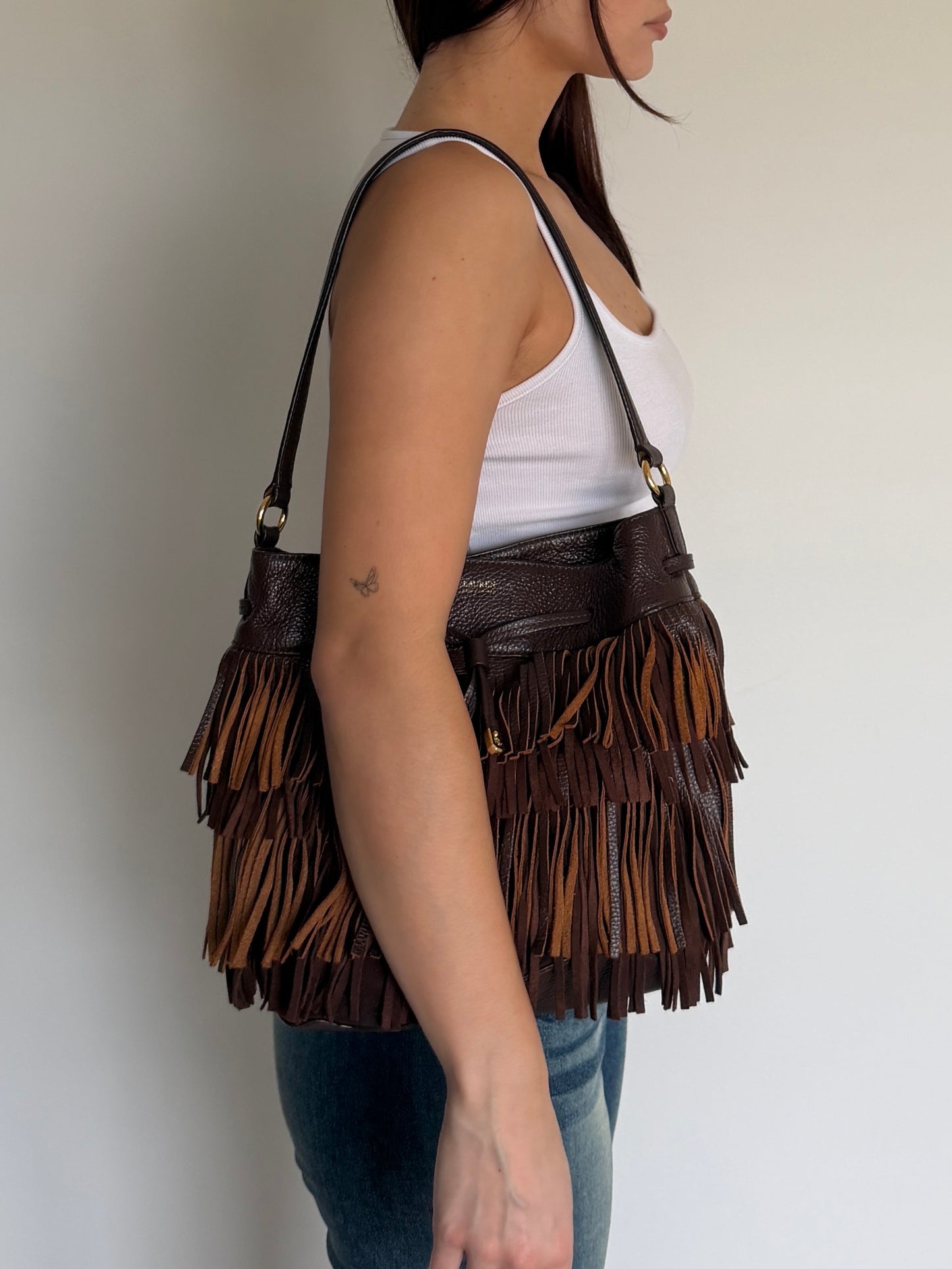 Person wearing a brown fringed handbag against a plain background