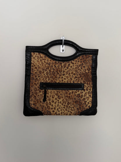 A leopard print handbag with black faux-leather trim and a top handle, hanging on a light gray wall.