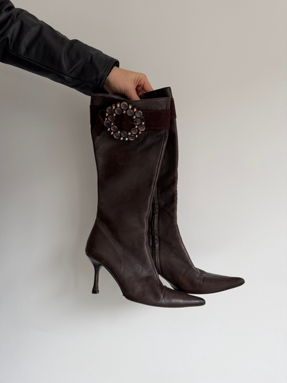 Brown knee-high boots with a decorative brooch on a light gray background