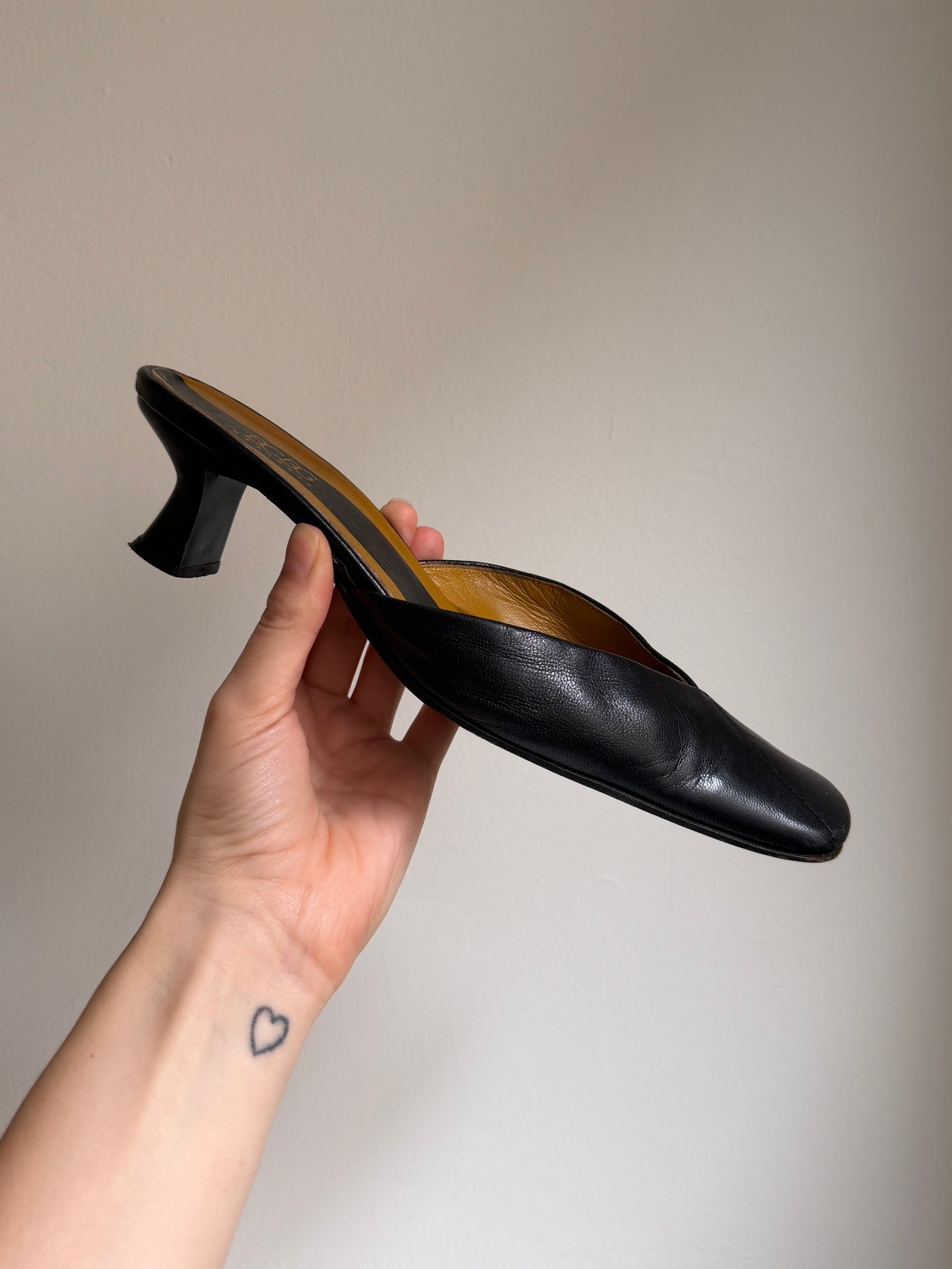 Hand holding a black high-heeled shoe against a plain background