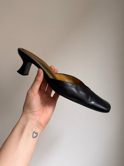 Hand holding a black high-heeled shoe against a plain background