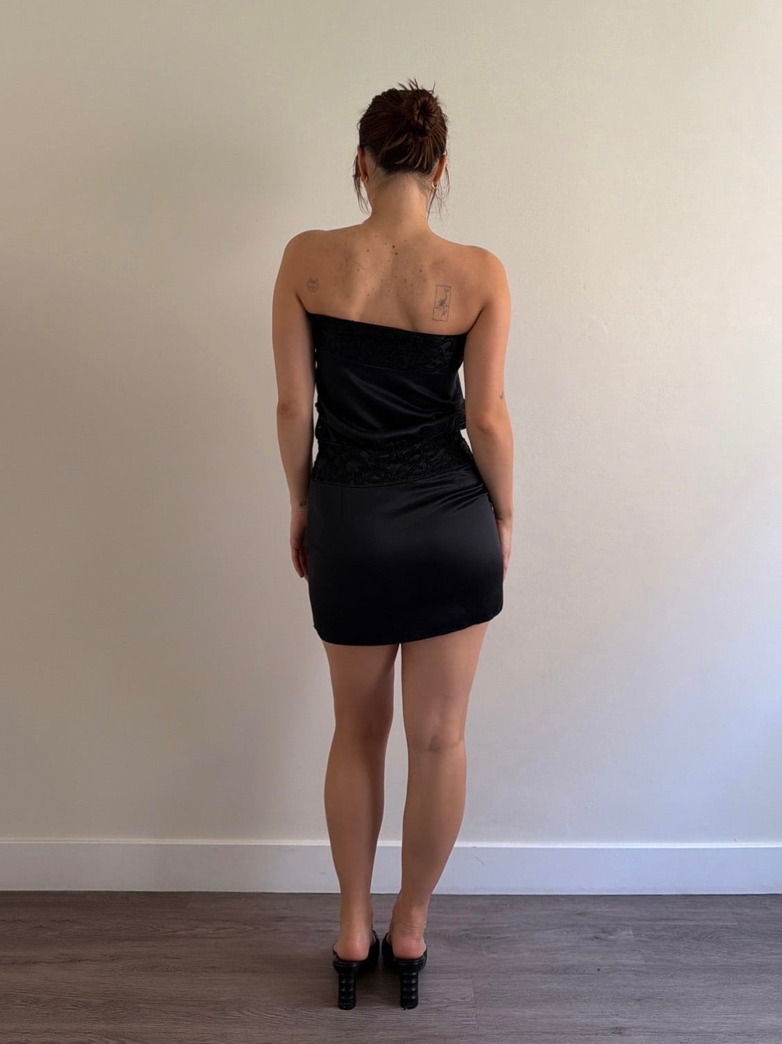 Person wearing a black strapless dress standing against a plain wall.