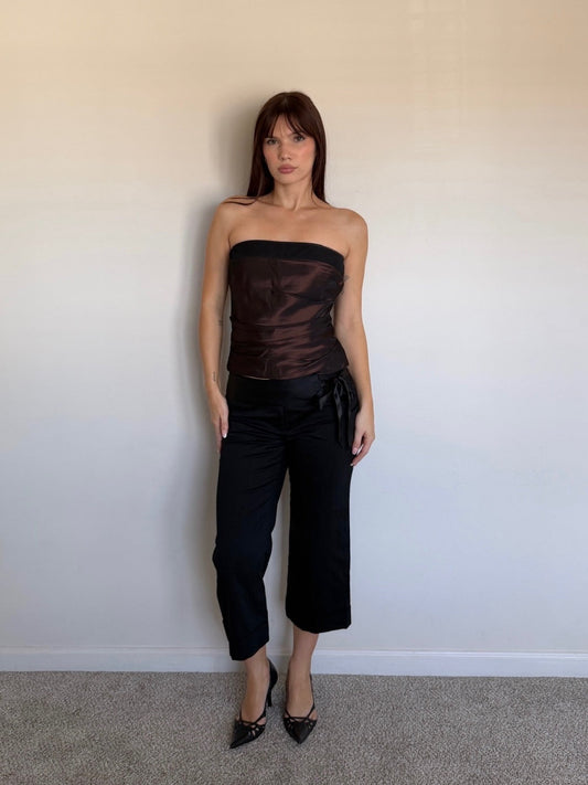 Person wearing a black strapless top and black pants against a plain wall.