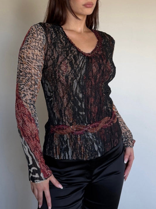 Woman wearing a patterned top and black pants against a plain background