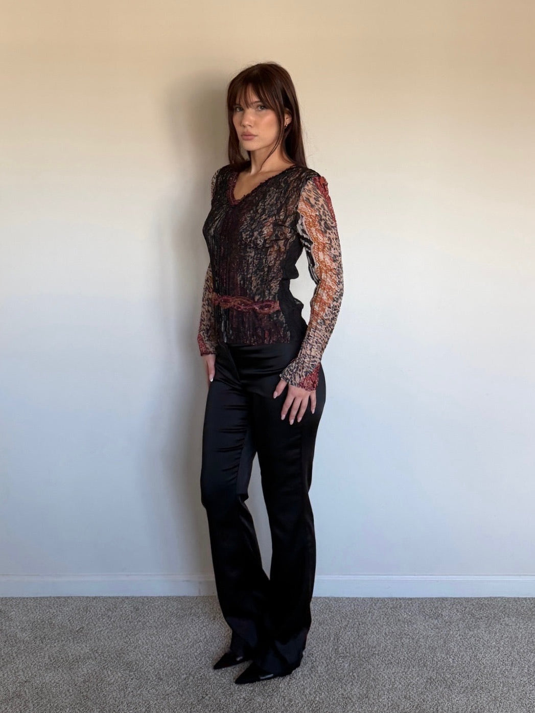 Person wearing a black lace top and black pants against a plain wall.