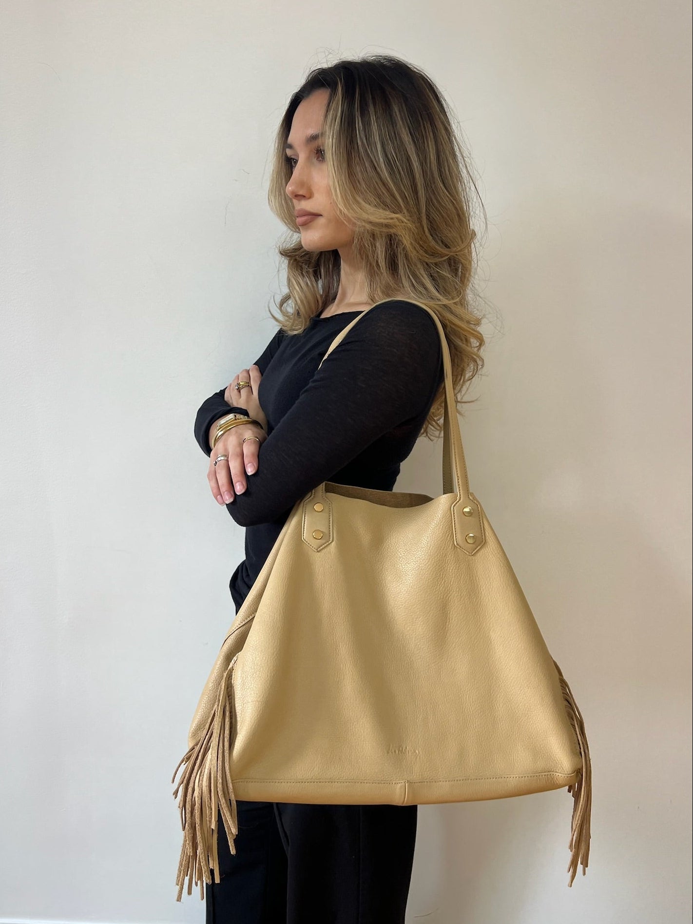 Woman holding a gold leather handbag with fringe details against a plain background
