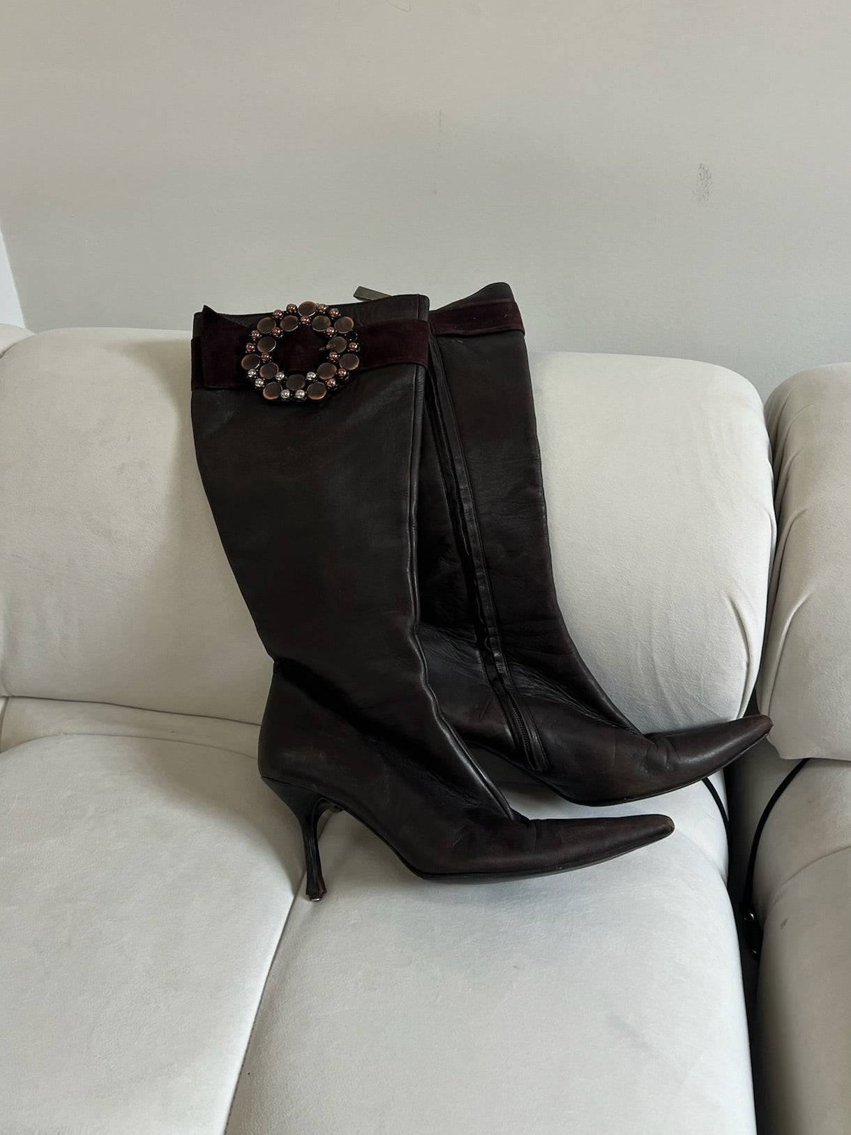 Brown knee-high boots with a decorative buckle on a beige couch.