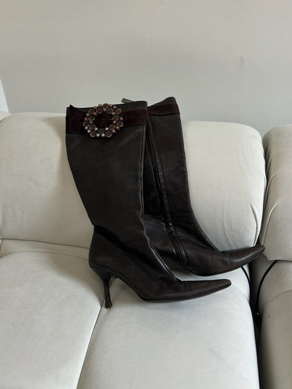 Brown knee-high boots with a decorative buckle on a beige couch.