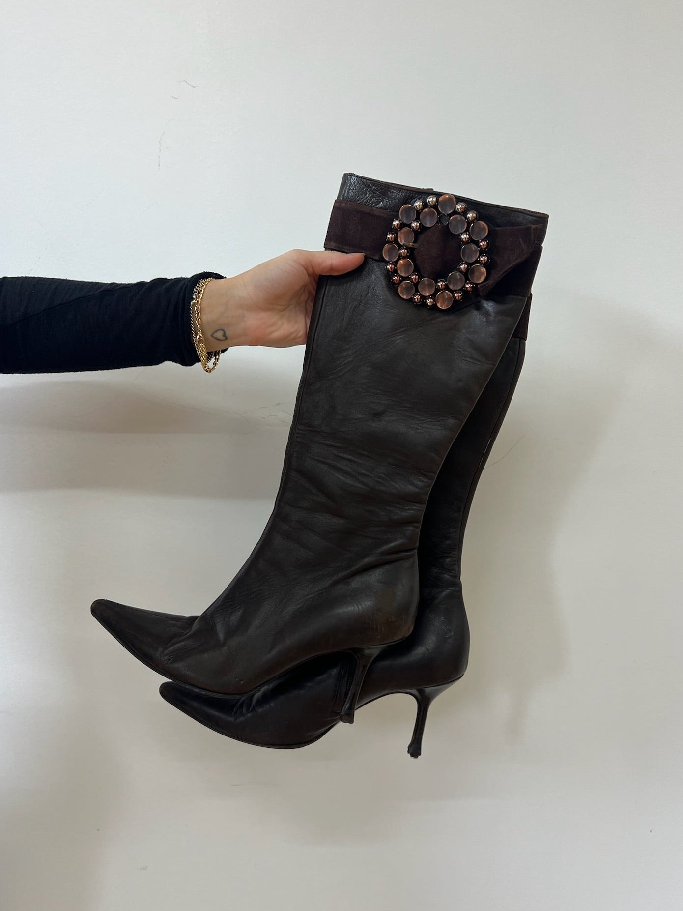 Brown leather boot with decorative buckle held by a hand against a white background