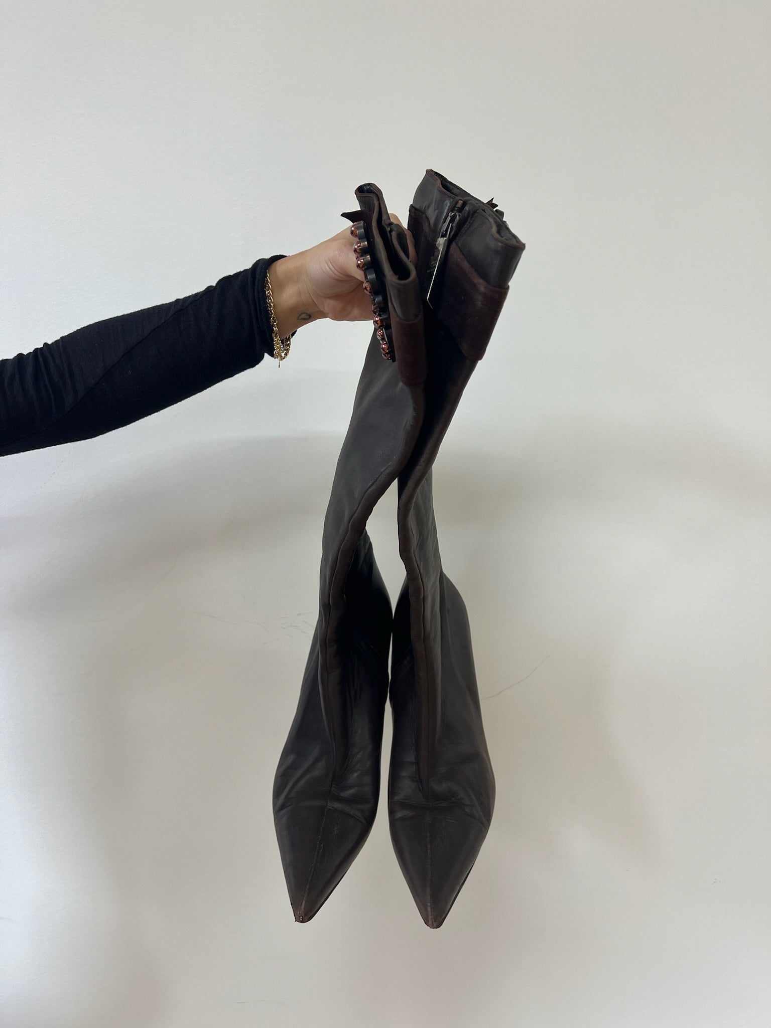Person holding a pair of brown leather boots against a white background