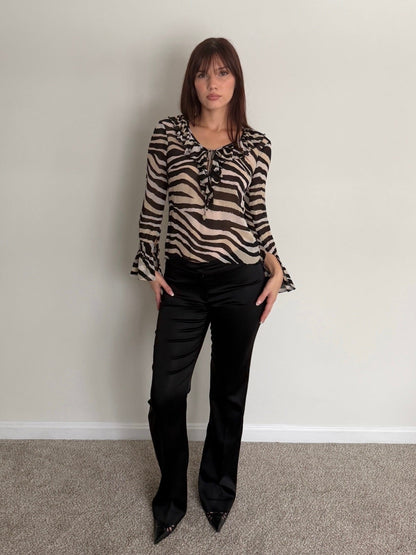 Woman wearing a zebra print blouse and black pants against a plain wall.