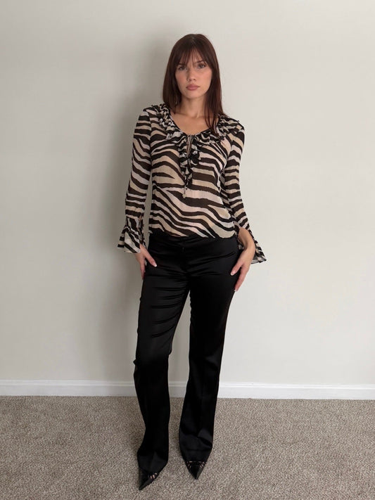 Woman wearing a zebra print blouse and black pants against a plain wall.