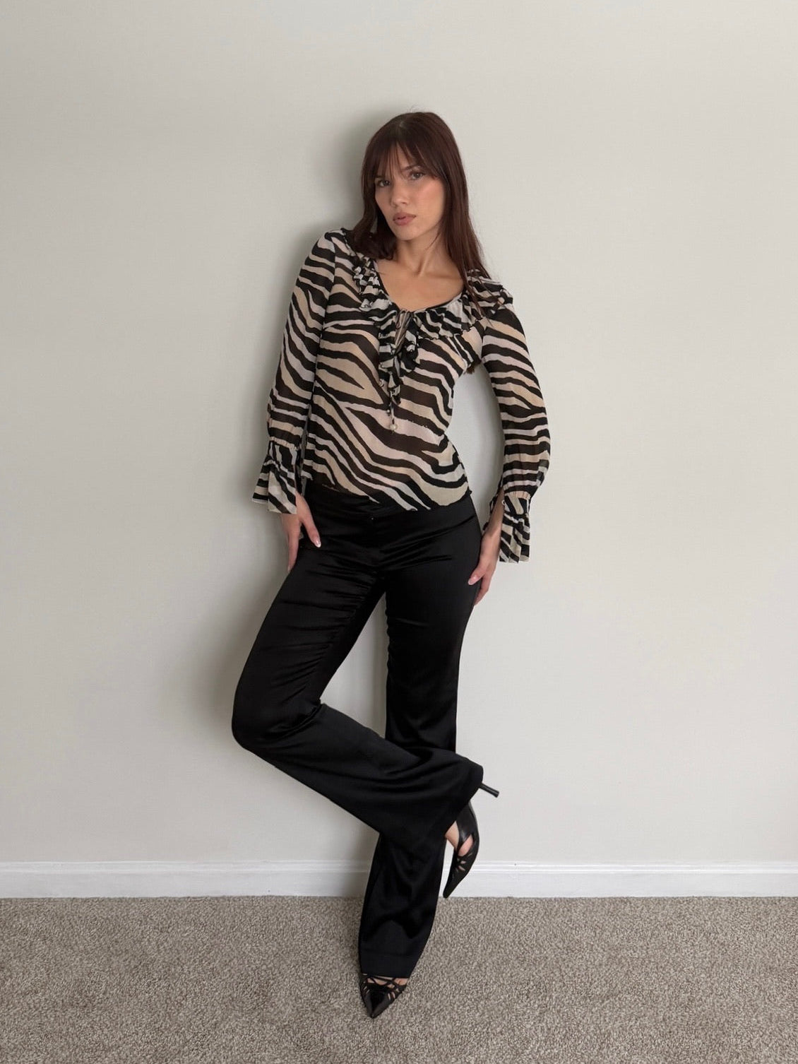 Woman wearing a zebra print blouse and black pants against a plain wall.