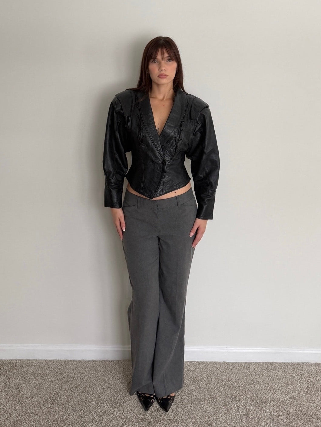 Person wearing a black satin jacket and gray pants against a plain wall.