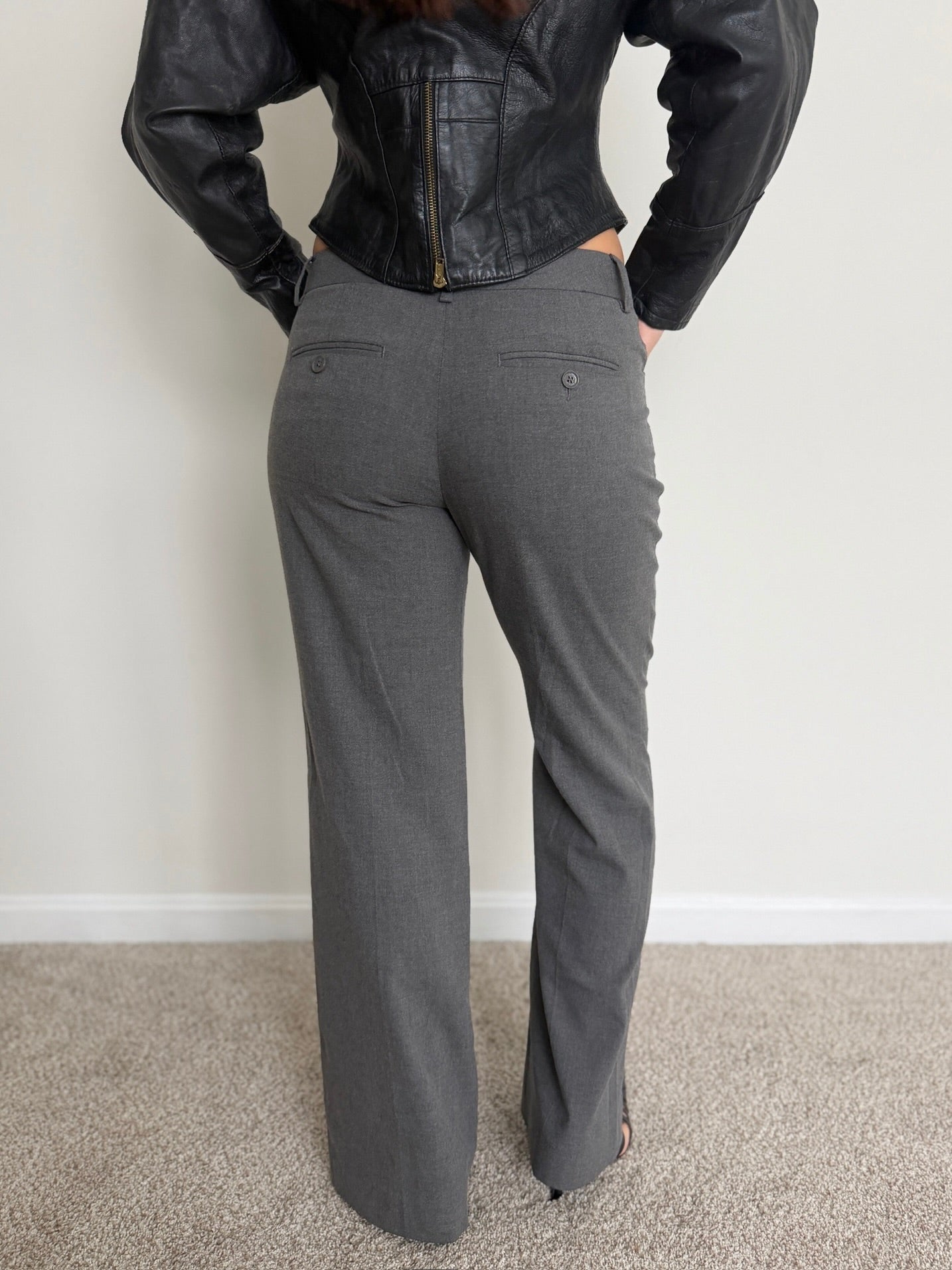 Person wearing a black leather jacket and gray pants against a white wall.