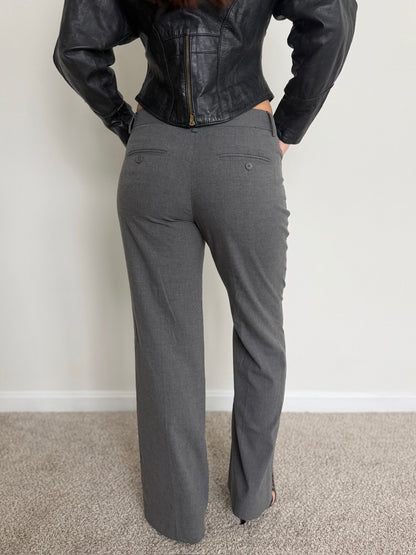 Person wearing a black leather jacket and gray pants against a white wall.