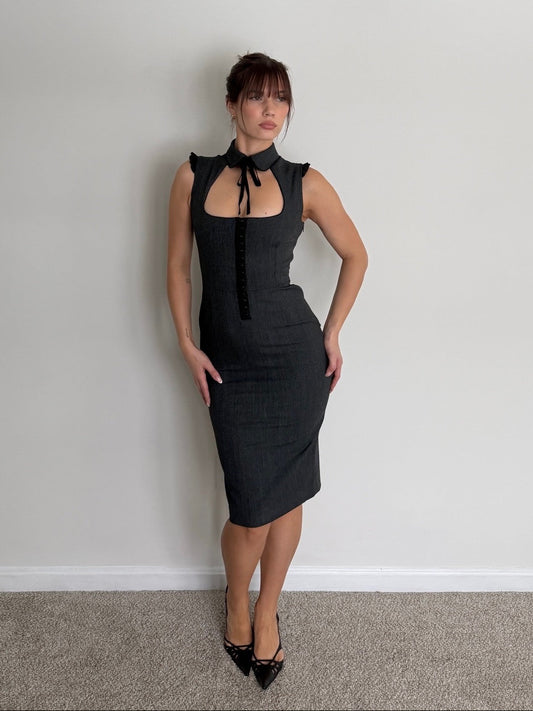 Woman wearing a black dress against a plain wall.