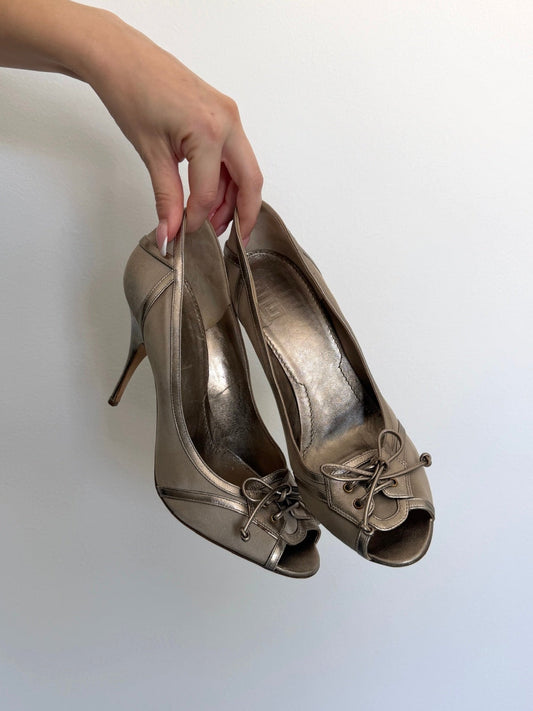 Pair of metallic high-heeled shoes held by a hand against a light background