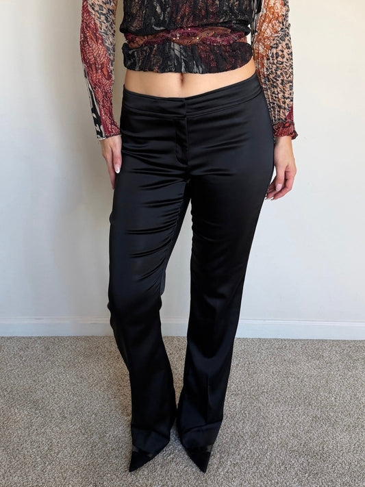 Person wearing a patterned top and black pants against a plain background